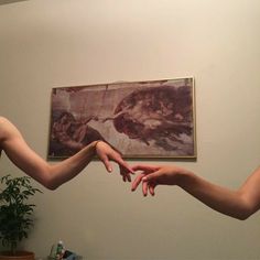 two hands reaching out towards each other in front of a painting on the wall behind them