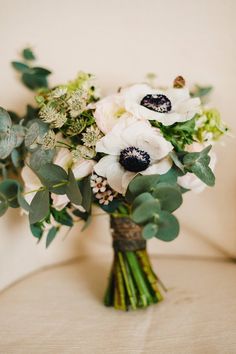 a bouquet of white flowers and greenery on a chair with a beige wall in the background