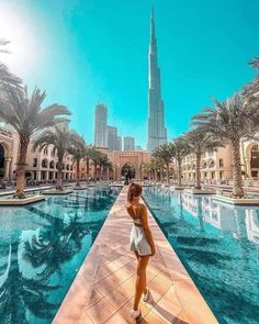 a woman standing on the edge of a swimming pool in front of a tall building