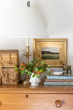 a white vase with flowers on top of a table next to books and a lamp