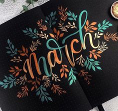 an open notebook with the word march written in gold and green lettering on it next to a cup of coffee