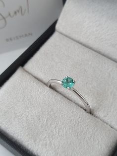 an engagement ring with a green stone sits in a box on top of a white surface