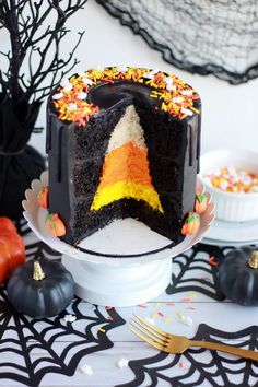 a halloween cake decorated with candy and sprinkles on a white plate next to black pumpkins