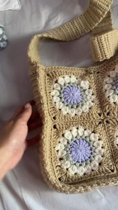 a crocheted purse being held up by someone's hand on a bed