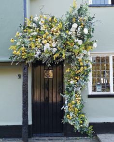 a black door with yellow and white flowers hanging from it's side next to a tree