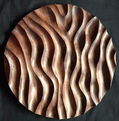 a wooden plate that has wavy designs on the front and back of it, sitting on a black surface