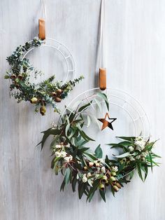 two circular wreaths hanging from hooks on a wall with greenery and star decorations