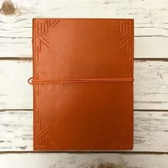 a brown leather notebook with an orange string attached to the cover on a white wooden background