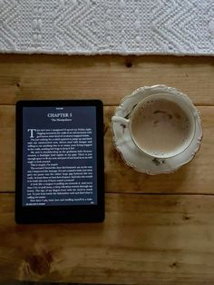 a cup of coffee next to an electronic book on a wooden table with a white towel