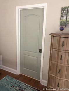 an empty room with a white door and dresser in the corner, next to a blue rug