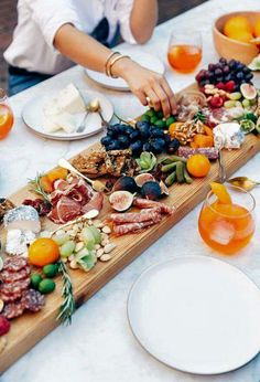 two people are serving food on a long wooden platter with oranges and grapes