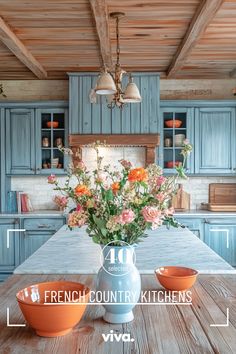 an image of a kitchen setting with flowers in the vase on the table and blue cabinets