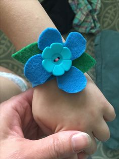 a hand holding a blue flower with green leaves on it's side and the other hand