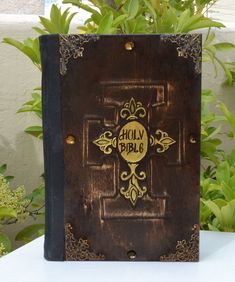 an old bible sitting on top of a white table next to some plants and flowers