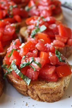 several pieces of bread with tomatoes and basil on top, sitting on a white plate