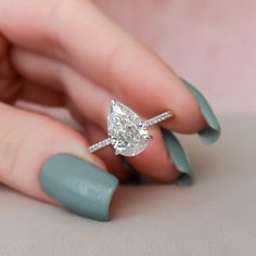 a woman's hand holding a ring with a pear shaped diamond on top of it