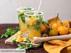 two glasses filled with lemonade and mint on top of a cutting board next to oranges