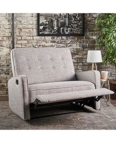 a gray couch sitting on top of a rug in front of a brick wall with a lamp next to it