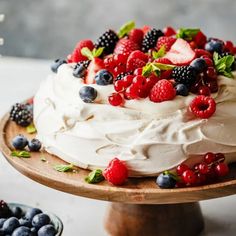 a cake with berries, raspberries and blueberries on top sitting on a wooden plate