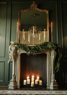 candles are lit in front of an ornate fireplace with greenery on the mantel