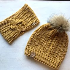 two knitted hats sitting next to each other on top of a white table with a brown pom - pom