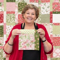 a woman holding up a piece of paper in front of a quilt