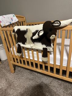 a crocheted cow blanket on top of a wooden crib next to a baby's bed