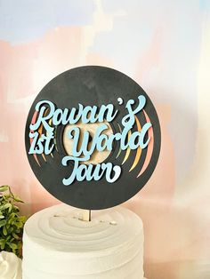 a cake with a sign that says rowan's 1st world tour on it next to a potted plant