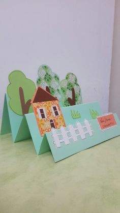 two cards with houses and trees on them sitting on top of a green tablecloth