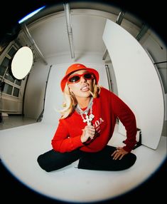 a woman sitting on the ground wearing sunglasses and a red hoodie is making a funny face