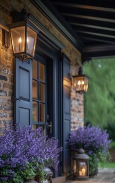 purple flowers in front of a house with two lanterns on the porch and an open door