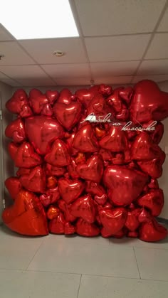 a large pile of red heart balloons sitting on top of a tiled floor next to a wall