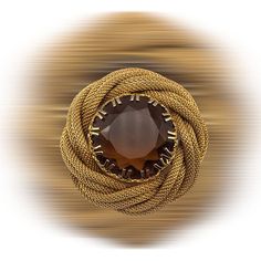 If you love the showy but elegantly made jewelry, this brooch is for you! The beautiful central stone is un-foiled, its topaz brown color is enhanced by the light that passes through it and by the facets It is inserted in a rich golden frame, a twisted effect of the tubular mesh chain  that creates around the stone a comfortable and voluptuous nest where to stay, protected by the decorative prongs The brooch does not show signatures or brands, but the quality is high and its vintage conditions are really excellent, no trace of a past is shown by the golden finish that feature clean surface and without stains, the crystal stone is also limpid and without chipping The pin measures cm.4,5 (1-3/4") in diameter the central stone is 25mm (1") It weighs 29 grams Dated c.1950s/1960s Secured by  ro Vintage Gemstone Round Brooches, Vintage Gemstone Brooches For Formal Occasions, Antique Jeweled Brooches For Formal Occasions, Formal Gold Gemstone Brooches, Elegant Brown Formal Brooches, Elegant Gold Brooches With Gemstones, Formal Round Gemstone Brooches, Unique Gemstone Brooch For Formal Wear, Elegant Gold Gemstone Brooches