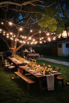 Outdoor dining setup with a long wooden table adorned with flowers and lights strung above, creating a cozy evening ambiance under a large tree. Outdoor Patio Birthday Party Ideas, Cabin Party Ideas, Backyard Setup Ideas, Patio Party Ideas Outdoor, Small Dinner Party Ideas Decor, Backyard Party Setup Ideas, Outdoor Night Party, Backyard Birthday Party For Adults, Outdoor Party Setup