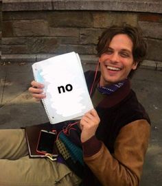 a man holding up a notebook with the word no written on it