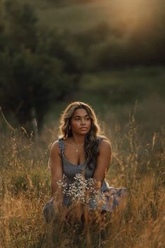 a woman sitting in tall grass with the sun shining down on her face and shoulders