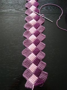 a purple and white crochet piece next to a ball of yarn