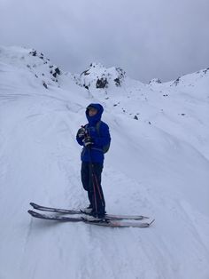 a person standing on skis in the snow near a snowy mountain side with mountains behind them