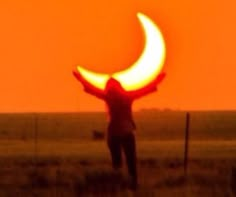 a person standing in a field with their arms up to the sky, and an orange sun behind them