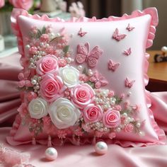 a decorative pillow with pink and white flowers on it, sitting on a table next to pearls