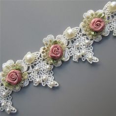 a white lace with pink roses and pearls on it's side is laying on a gray surface