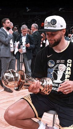 a man sitting on top of a basketball court while holding two trophies in his hands