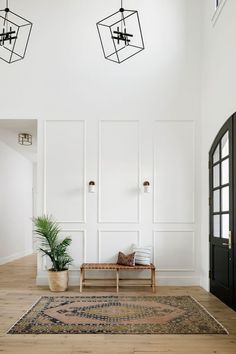 a living room with white walls and wooden floors, an area rug and two hanging lights