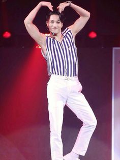 a man in striped shirt and white pants standing on stage with his hands behind his head