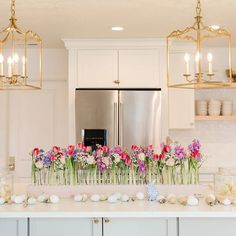 a kitchen counter with flowers in vases and candles on the counter top next to an open refrigerator