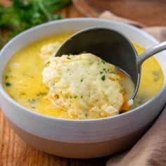 a white bowl filled with soup on top of a wooden table next to a spoon