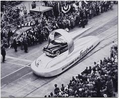 an old photo of a car in the middle of a parade with people watching it