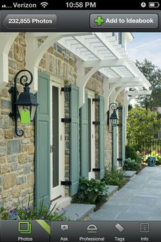 the front entrance to a house with green shutters and blue doors, surrounded by flowers