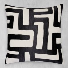 a black and white pillow sitting on top of a gray wall next to a plant