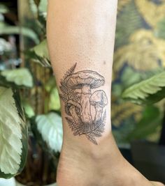 a person with a mushroom tattoo on their leg and foot is standing in front of a potted plant